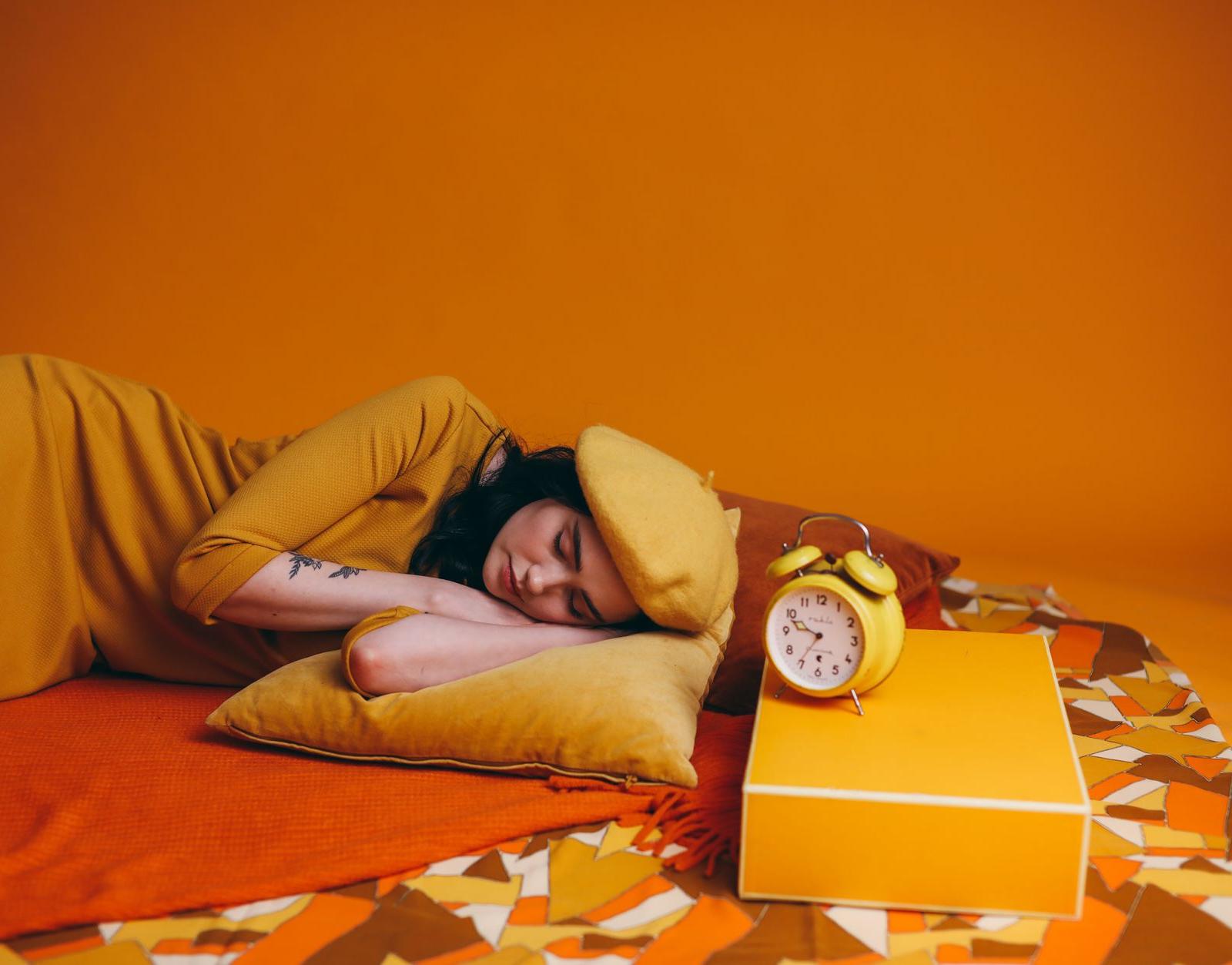 Woman in Yellow Outfit Lying Down beside an Alarm Clock